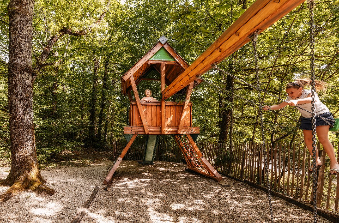 Une enfant assise dans la cabane perchée, une autre sur la balançoire