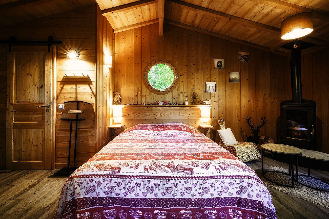 La chambre de la Cabane Balnéo : le lit, le poêle à bois et le hublot
